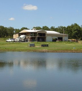 Photo of a big barn with a pond in foreground.